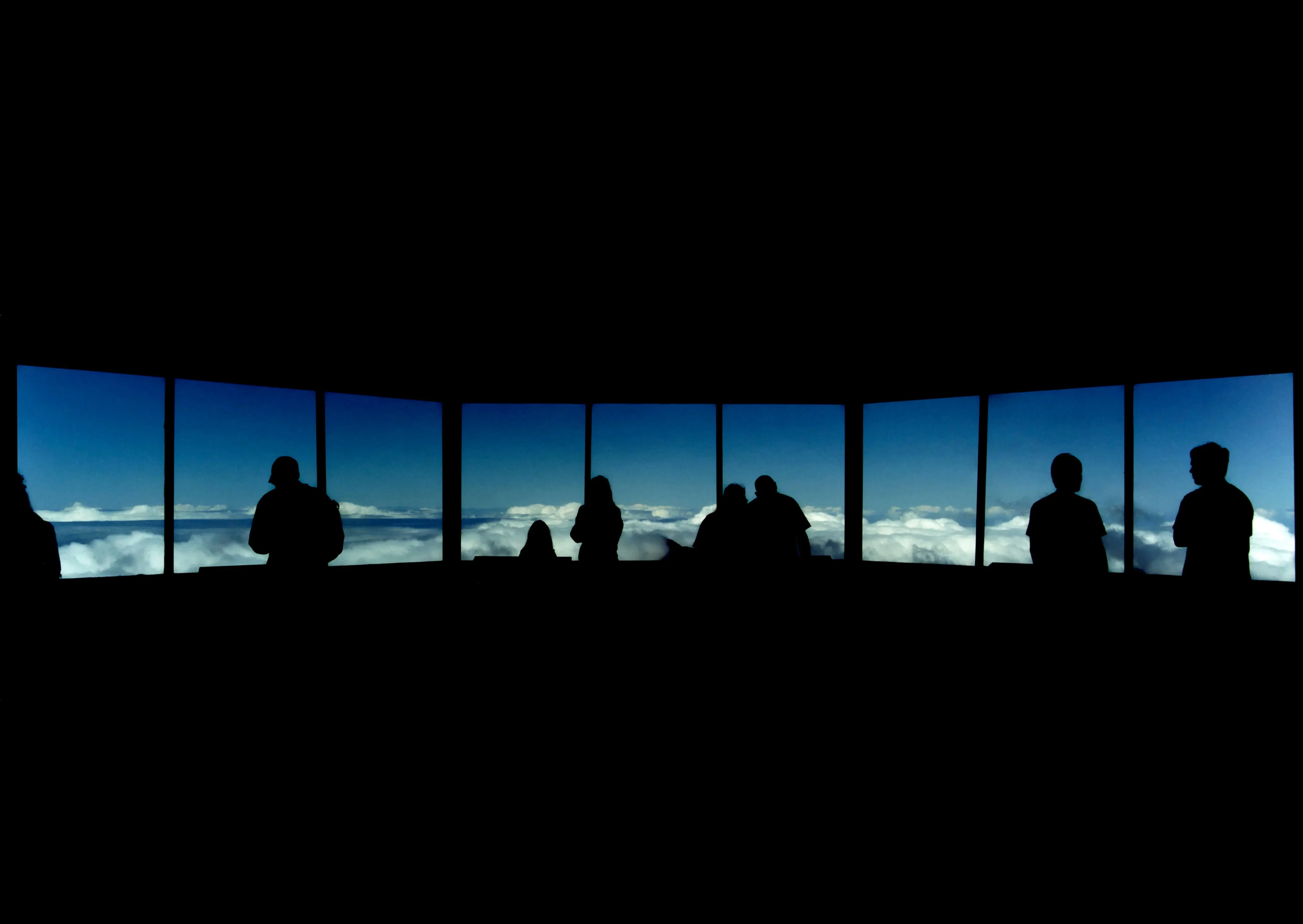 A group of silhouetted people look out windows at a blue sky with clouds